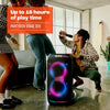 A group of friends dancing outdoors next to a JBL PartyBox Stage 320 with its telescopic handle and wheels visible, displaying colorful LED lights.