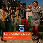 A group of friends dancing outdoors next to a JBL PartyBox Stage 320 with its telescopic handle and wheels visible, displaying colorful LED lights.