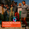 A group of friends dancing outdoors next to a JBL PartyBox Stage 320 with its telescopic handle and wheels visible, displaying colorful LED lights.