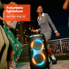 “A group of friends dancing outdoors next to a JBL PartyBox Stage 320 with its telescopic handle and wheels visible, displaying colorful LED lights.”