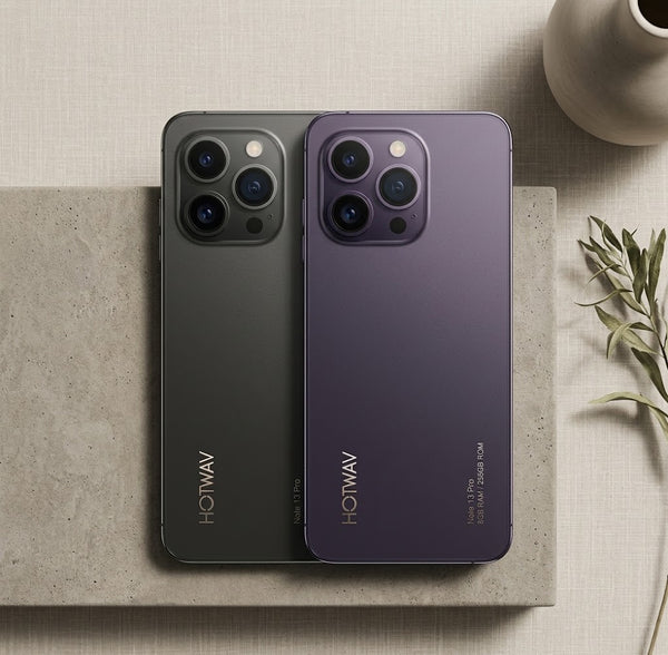 Two HOTWAV smartphones shown from the back, one in dark gray and one in deep purple, placed on a textured stone slab with a neutral beige background and decorative props.
