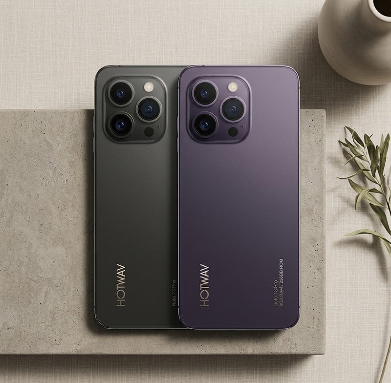 Two HOTWAV smartphones shown from the back, one in dark gray and one in deep purple, placed on a textured stone slab with a neutral beige background and decorative props.